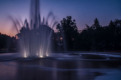 Illuminated fountain against sky at sunset