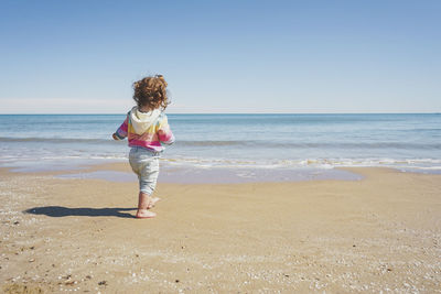 Rear view of woman standing at beach against clear sky