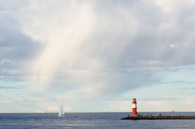 Lighthouse amidst sea against cloudy sky