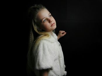 Side view of thoughtful girl looking away while standing against black background
