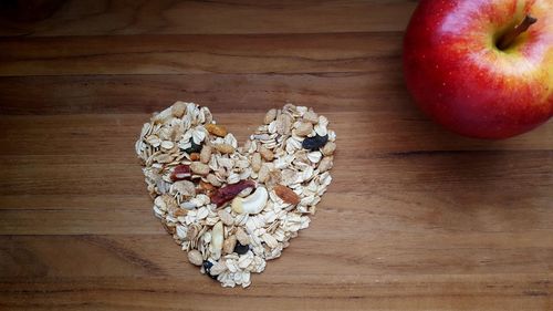 High angle view of heart shape made from breakfast cereals by apple on wooden table