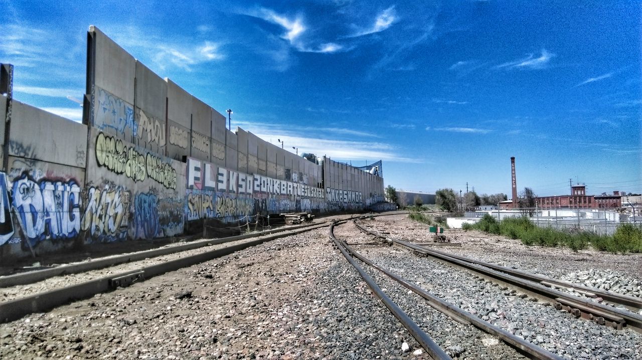 railroad track, transportation, rail transportation, public transportation, railroad station platform, railroad station, sky, blue, text, railway track, built structure, the way forward, diminishing perspective, train - vehicle, cloud - sky, no people, building exterior, architecture, day, travel