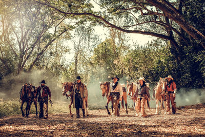 Men with horses walking on land in forest