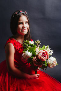 Portrait of girl holding bouquet while kneeling against black background