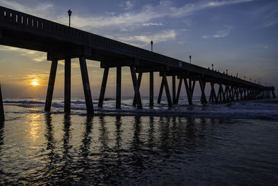 Silhouette bridge over sea against sky during sunset