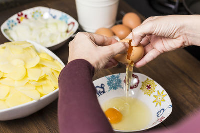Cropped hands of woman breaking eggs in bowl on table