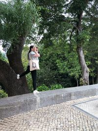 Woman standing on footpath by tree