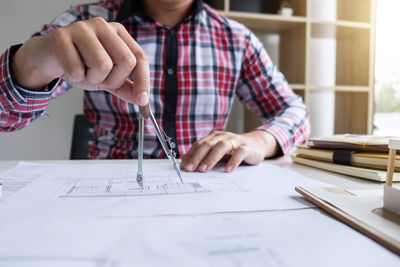 Midsection of architect drawing blueprint on paper in office