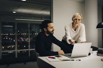 Male and female professionals planning strategy while discussing over laptop in illuminated office