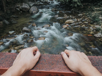 Hands of man on railing over stream in forest