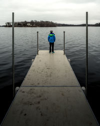 Rear view of boy standing on pier over lake against sky