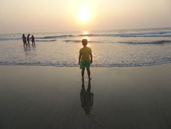 Rear view of men on beach against sky during sunset