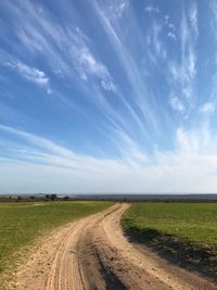 Dirt road amidst field against sky