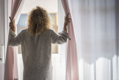 Rear view of woman standing by window at home