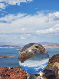 Close-up of crystal ball against water and sky