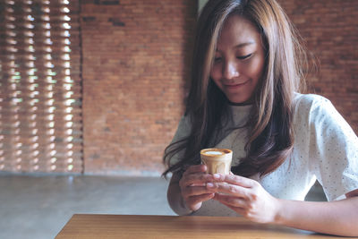Smiling woman holding coffee while sitting at table in cafe