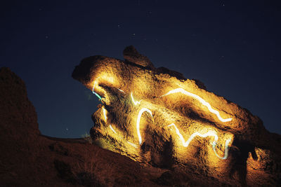 Low angle view of illuminated rock formation against sky at night