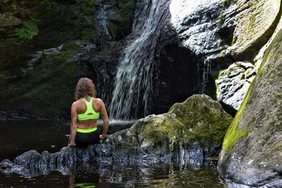 Rear view of woman wearing sports bra against waterfall