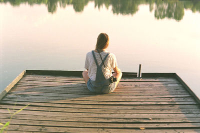 Rear view of woman sitting on pier at lake