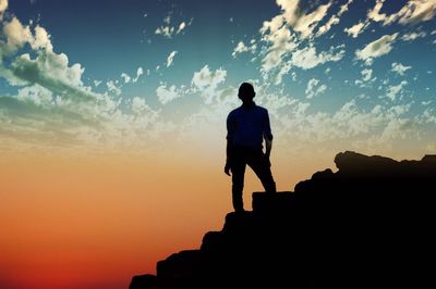 Man standing on rock against sky during sunset