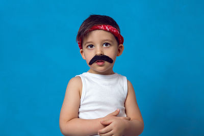 Small boy with a false mustache in a white t-shirt and a red headband on a blue background