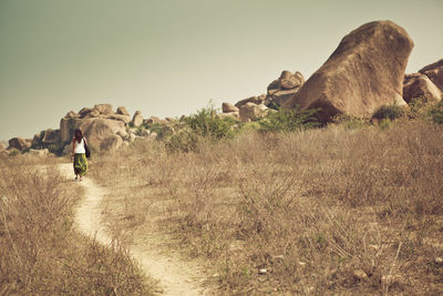 Rear view full length of woman on walkway by grassy field against sky