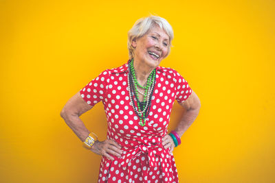 Smiling senior woman standing against yellow background