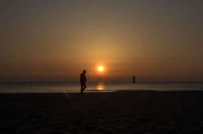 Silhouette man walking on shore at beach against sky during sunrise