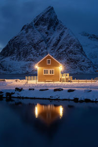 Illuminated buildings by mountain against sky during winter