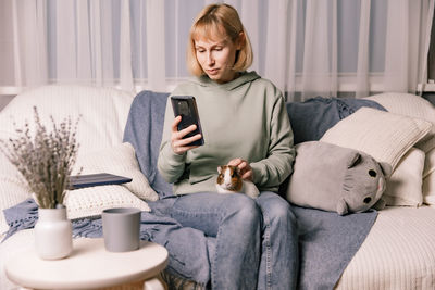 Young woman using phone while sitting on sofa at home