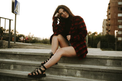 Full length of young woman sitting on steps in city