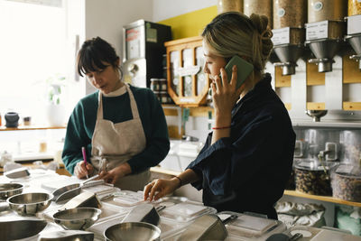 Owner talking on smart phone while colleague taking inventory in store