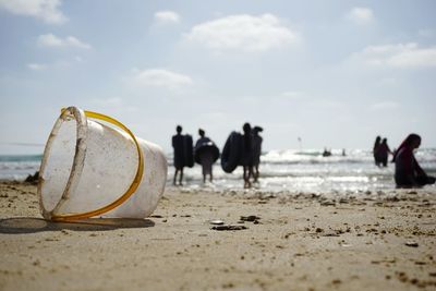 Bucket by people at beach against sky