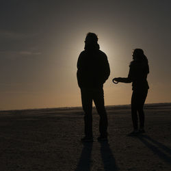 Silhouette couple standing on beach against sky during sunset