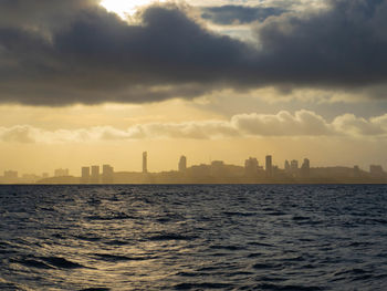 Sea by buildings against sky during sunset