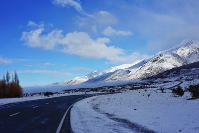 Road by snowcapped mountains against sky during winter