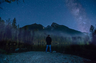 Rear view of man standing on land against sky at night