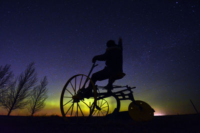 Low angle view of man riding on tricycle against sky with aurora at night