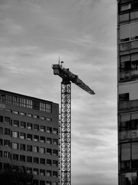 Low angle view of crane by building against sky