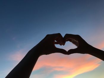 Close-up of silhouette hand holding heart shape against sky during sunset