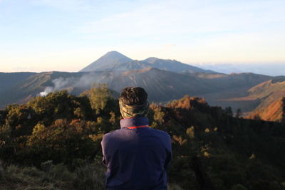 Rear view of man looking at mountains against sky