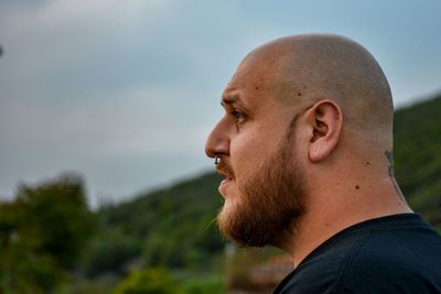 Side view of handsome bald bearded man against sky