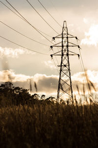 Electricity pylon in field against cloudy sky