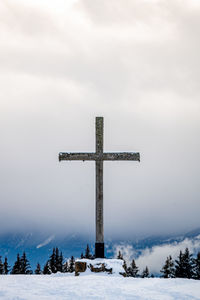 View of cross on snow covered landscape against sky