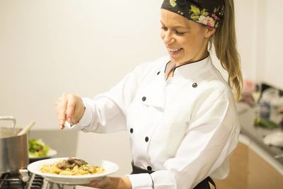 Happy female chef garnishing pasta in plate at commercial kitchen