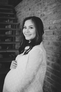 Portrait of smiling young woman standing against brick wall