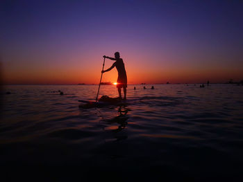 Silhouette man standing in sea against sky during sunset