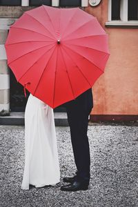 Midsection of woman with umbrella standing against the wall