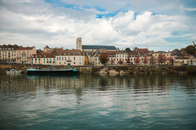 Scenic view of river by cityscape against sky