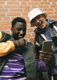 Low angle view of happy male friends laughing while sharing smart phone with each other